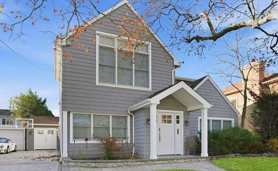 Gray two-story coastal home with dark shingle roof, white trim, front gable entry, and large windows, showing a clean residential roofing exterior.
